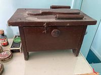 Front view of vintage wooden shoe shine kit box with contoured shoe shape on top and front storage drawer.