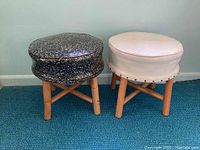 Two stools side-by-side, left is black speckled vinyl top and right is plain white vinyl top, both have wooden legs and cross braces.