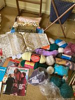 Full view of yarn skeins, sewing patterns, fabric pieces, and fabric basket stand on floor.