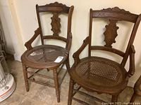 Two antique Victorian carved wooden dining accent chairs with cane seats, one seat torn and with visible mold.