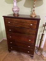 Front view of the dark wood chest of drawers with four drawers and metal knobs, showing one knob missing and surface scratches.