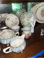 Porcelain creamers and sugar bowl with floral patterns, miniature bone china flower baskets and a decorative hand figurine