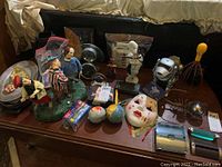 Wide view of lot showing diverse items including clown mask, maracas, clocks, dolls, and robot dog toy on a wooden table