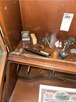 Display cabinet shelf featuring bronze baby shoes, miniature bicycles, Civil War miniatures, carved figurines, antique fountain pen, and other assorted collectibles.