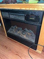 Front view of electric fireplace heater showing black metal front, simulated logs inside, and front control panel.