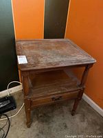 Full view of wooden end table showing top surface, drawer, lower shelf, and legs with visible scratches and worn finish.