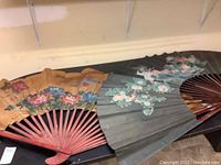 Two hand painted folding fans fully opened and displayed side by side showing painted floral designs and size