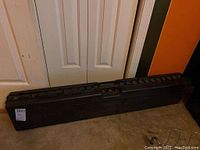 Closed view of black hunting case with detailed wildlife design on the front, placed against white doors and orange wall.