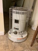 Full view of the Kero-Sun Omni 105 kerosene heater showing white cylindrical body with protective metal cage and base with warning labels.