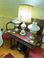 Two lamps on wooden console table; one lamp has a fabric shade, the other lamp shows the white glass oil lamp shade alone. Chairs and wooden furniture in background.