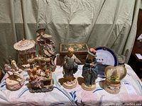 Wide view of all items showing four music boxes, four figurines, blue boy statue, chocolate box, and Titanic plate arranged on table