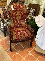 Front view of the Victorian era parlor chair showing the red and gold fabric upholstery and carved wooden frame