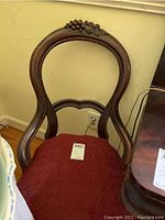 Full view of one Victorian wooden parlor chair showing curved back and red upholstery.