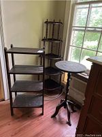 Full view of three pieces: black wooden rectangular shelving unit, corner shelf unit, and small round table