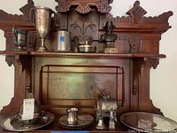 Wide view of entire lot showing antique wooden hutch with various silver-plated items including biscuit boxes, dishes, trophies, a cup, and a bust statue.