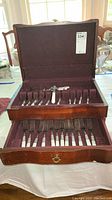Open wooden flatware case showing two layers of cutlery including forks and knives with mother of pearl handles.
