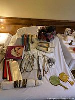 Wide view showing jewelry spread out on fabric, white slip-on shoes, beaded necklaces, bracelets, and earrings, along with a framed photo album or box alongside.