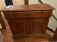 Wooden sideboard table viewed from front showing two drawers and two cabinet doors with metal hinges and handles, medium brown finish and some scratches.