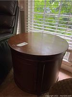 Front view of the circular wooden side table showing the top and storage cabinet below.