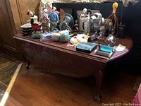 Dark wooden table shown with two 9-inch drop leaves visible on either side, with various collectible items on top. Several scratches and chipping are apparent on the table surface.