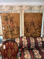 Two hanging tapestry panels displayed above floral and striped couch. Both tapestries in good condition, slightly folded at the top edge.