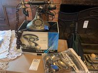 Brass-tone Nostalgic Duke rotary telephone on its original box with assorted metal drawer pulls nearby.