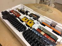 Train set components arranged in original white styrofoam tray, showing locomotive, train cars, and black curved track pieces.