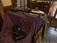 Photo showing both vacuums on a purple-draped surface, Dyson in blue and Black & Decker in black with visible cords and vacuum hoses.