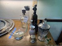 Large clear glass display bowl, several vases including black hourglass timer figure, and cut glass candy dish with lid.