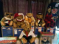 Photo of six Vermont Teddy Bears seated on their original branded blue boxes, showcasing various outfits and some accessories in a living room setting.