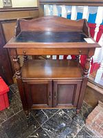 Front view of vintage wooden bar cart showing black top with drawer and two-door cabinet below