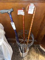Three walking sticks and cane standing in metal stand; two antique hand-carved bamboo Japanese walking sticks with tags and one Carex cane with grey handle