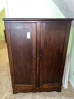 Front view of dark wooden wardrobe with two large paneled doors and central vertical molding, no keys in locks visible.
