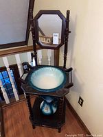 Overview of the wooden wash stand showing the attached octagonal mirror, ceramic basin on top, and ceramic pitcher on the bottom shelf.