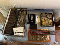 Overview of the entire lot showing ties, watch box, belt buckles, keychains, guitar strap, wallet, and belt hanger on table.