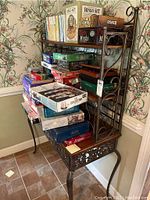 Photo showing full wine rack filled with various board games on shelves, highlighting the metal frame and carved wood elements