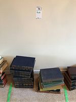 Photo showing multiple stacks of hardcover books placed on carpet under a wall marked 'Books 16'. Books show different sizes and some wear.