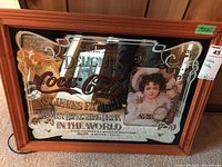 Full view of Coca Cola advertising mirror in wood frame with vintage text and portrait graphics.