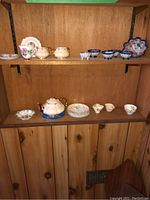 First photo showing multiple shelves with various porcelain dishware including teapot, creamer, sugar bowl, plates, and cups with floral and gold designs.