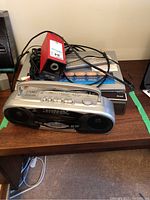 Photo shows a silver Citizen stereo boombox with built-in speakers, a red Sharp electric pencil sharpener, and a black Sony DVD player beneath. Various cables are visible as well.