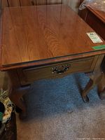 Top and angled views of wood veneer end table with one drawer and metal pull handle, displaying wood grain and curved legs