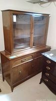 Full view of Knechtel China cabinet with wood and glass doors in a basement setting.