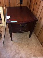 Front view of the wood end table showing rich brown finish, curved front, and brass handles on two drawers.