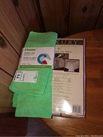 Green FRANK microfibre cloths pack on top of a packaged 12-piece luxury table set