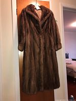 Front view of the full-length brown mink fur coat hanging on a door, showing its collar, invisible clip closure, and long length.