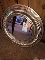 Front view of round mirror showing ribbed, metallic-colored plastic frame and reflective glass.