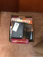 Top-down photo showing a box filled with various VHS and DVD cases including The Lord of the Rings VHS, True Grit VHS, Enchanted VHS, and other cases.