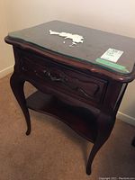 Front angled view of night table showing drawer closed, glass top with paper residue, curved legs