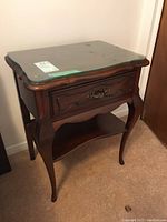 Front right view of night table showing curved legs, drawer, lower shelf and glass top