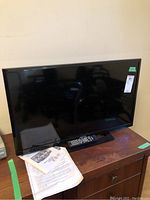 Black 32-inch flat-screen television with remote placed on wooden cabinet.